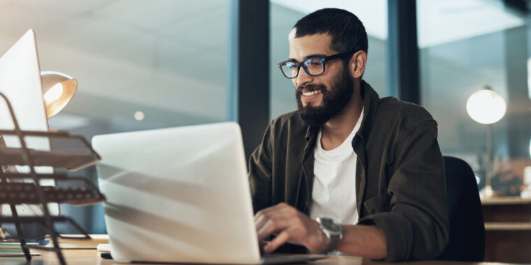 Shot of a young businessman using a laptop during a late night in a modern office